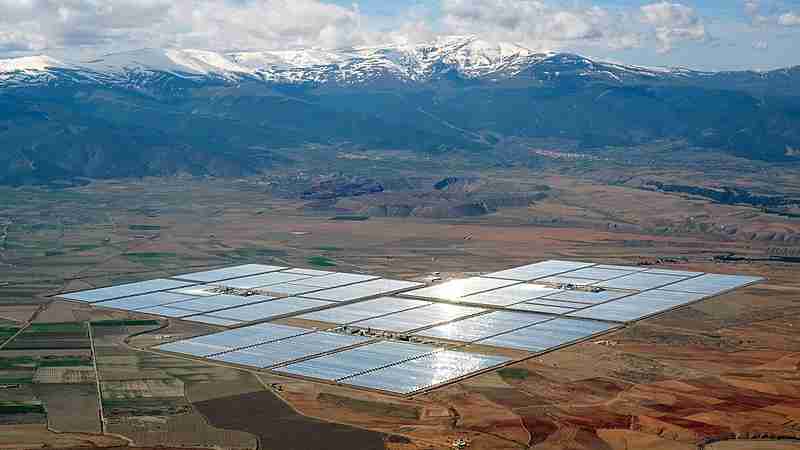 Renewable energy - Concentrated solar power parabolic troughs in the distance arranged in rectangles shining on a flat plain with snowy mountains in the background, tags: fearna sse und gilkes - CC BY-SA